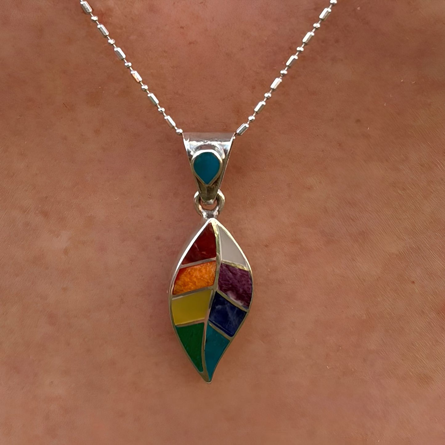 Pendentif Sylva porté de près avec motif feuille stylisée et pierres naturelles multicolores