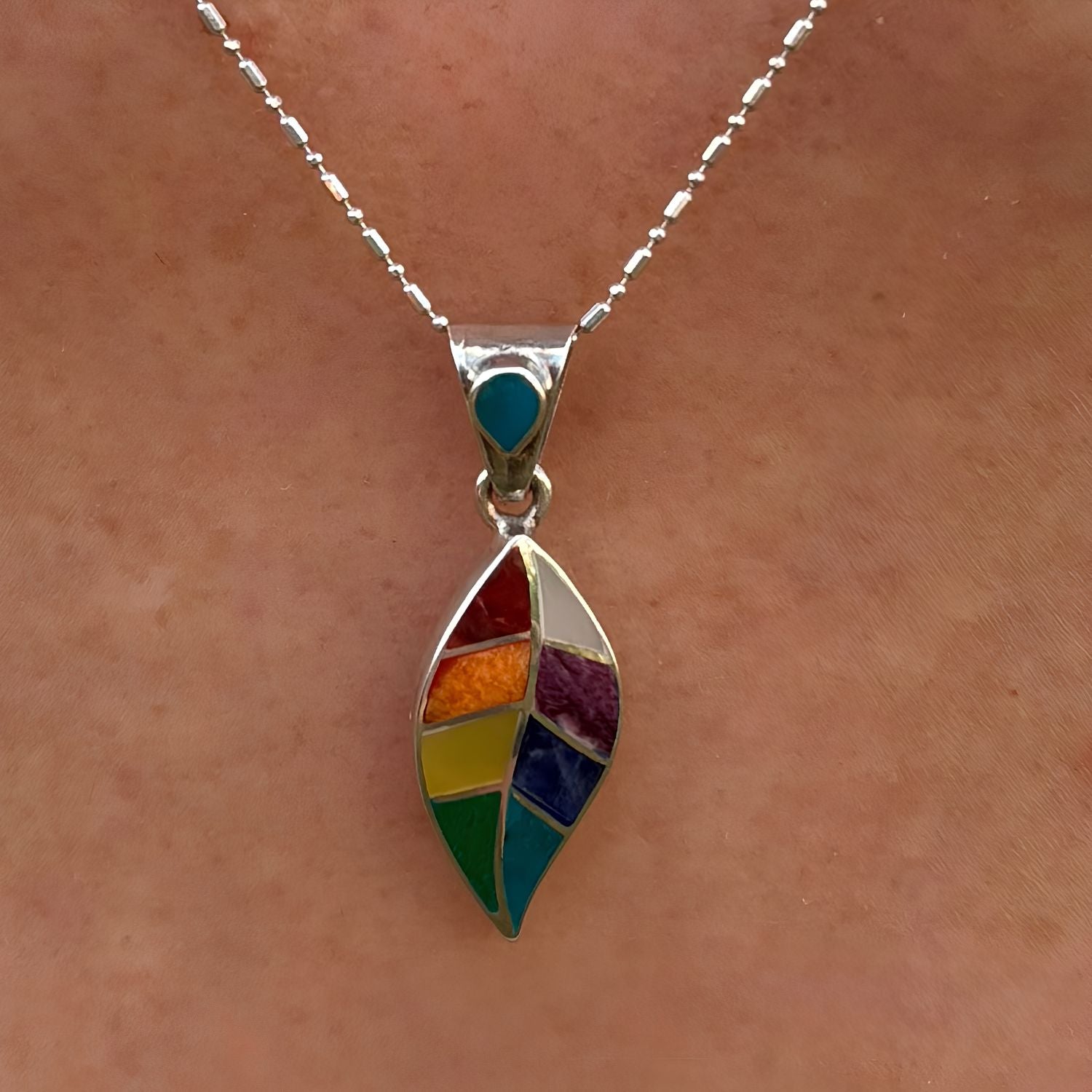 Pendentif Sylva porté de près avec motif feuille stylisée et pierres naturelles multicolores